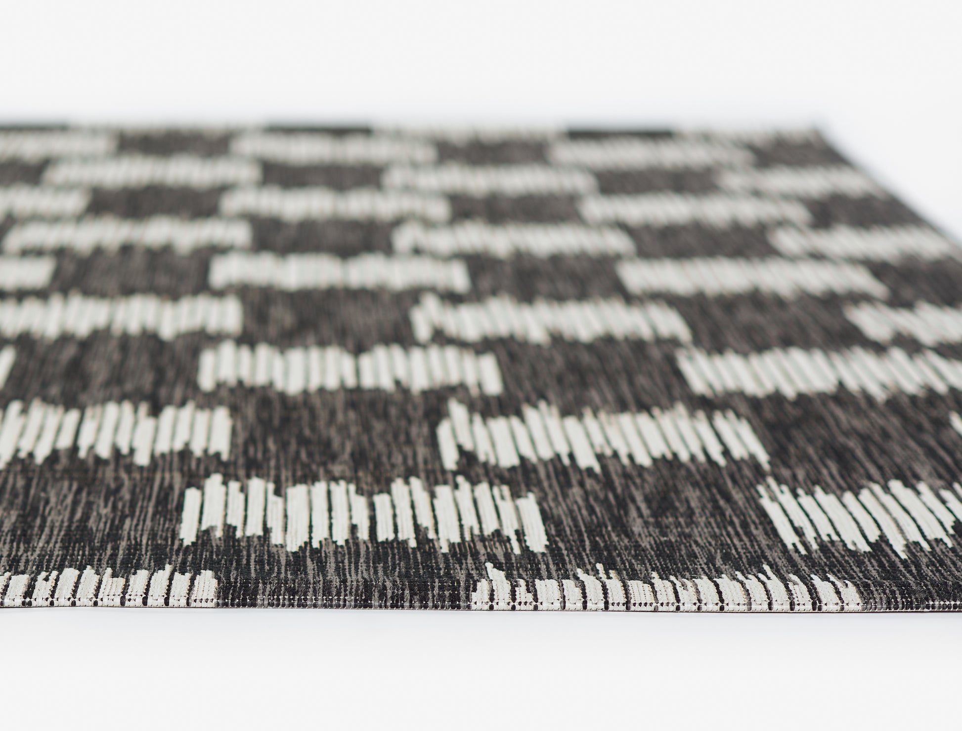 Close-up of a black and white woven rug with geometric rectangle pattern and fringe edge.