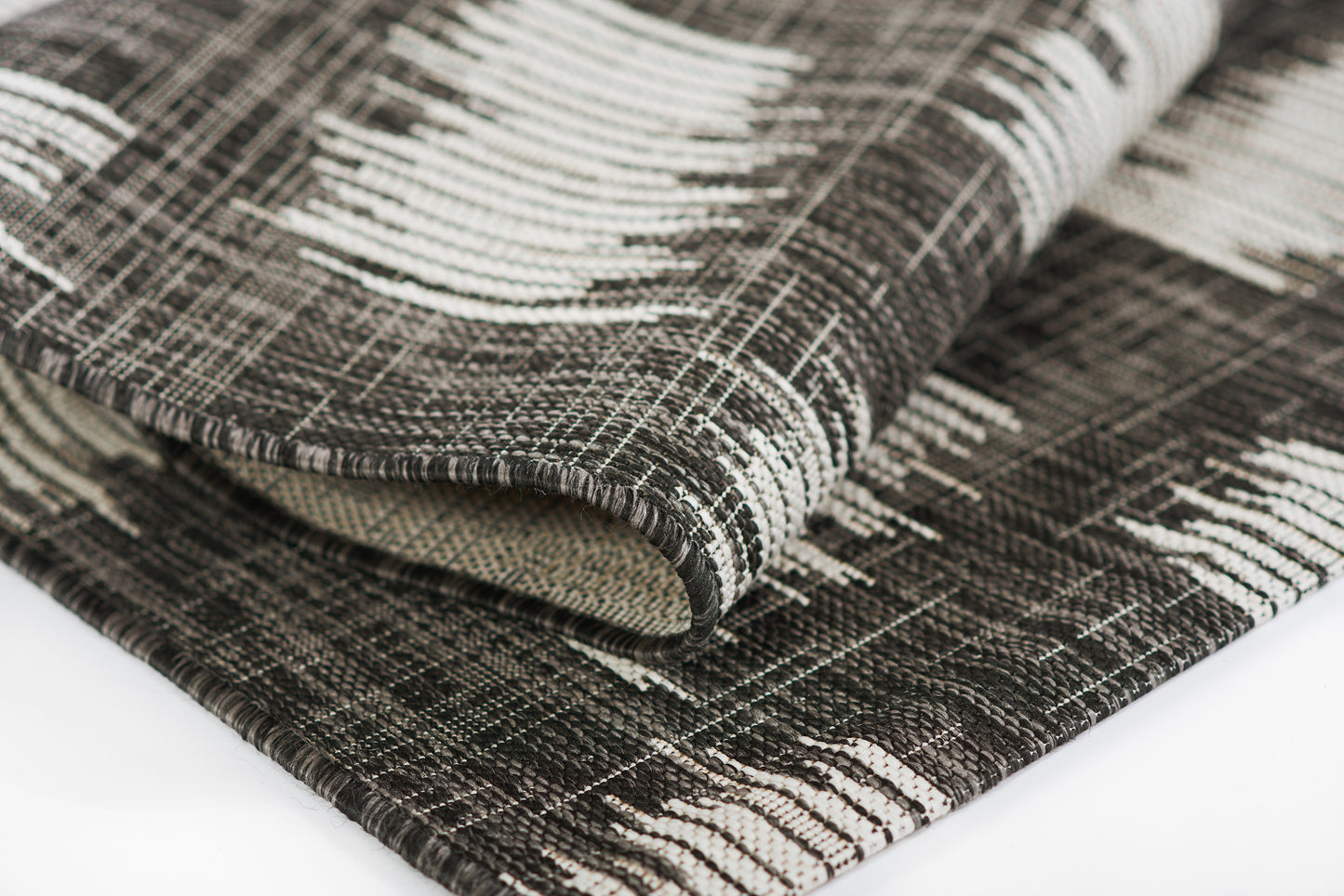 Folded black-and-white woven runner rug with geometric stripe pattern; thick textured textile for floor or throw; 3' x 8'.