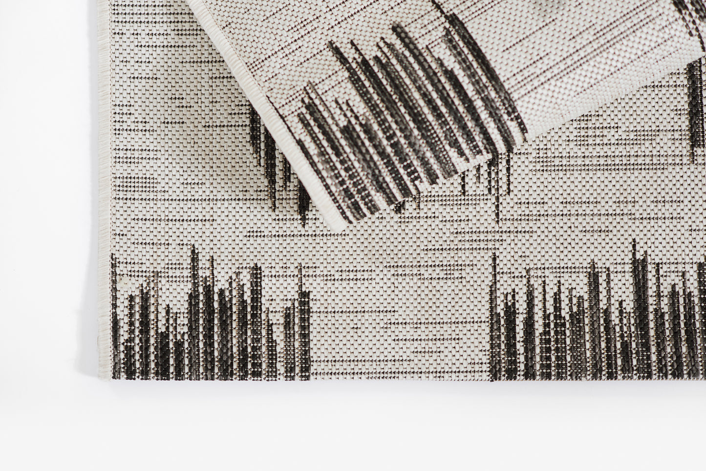 Ivory woven textile with bold black abstract linear pattern; rolled corner with fringe, ideal as a throw or wall decor.