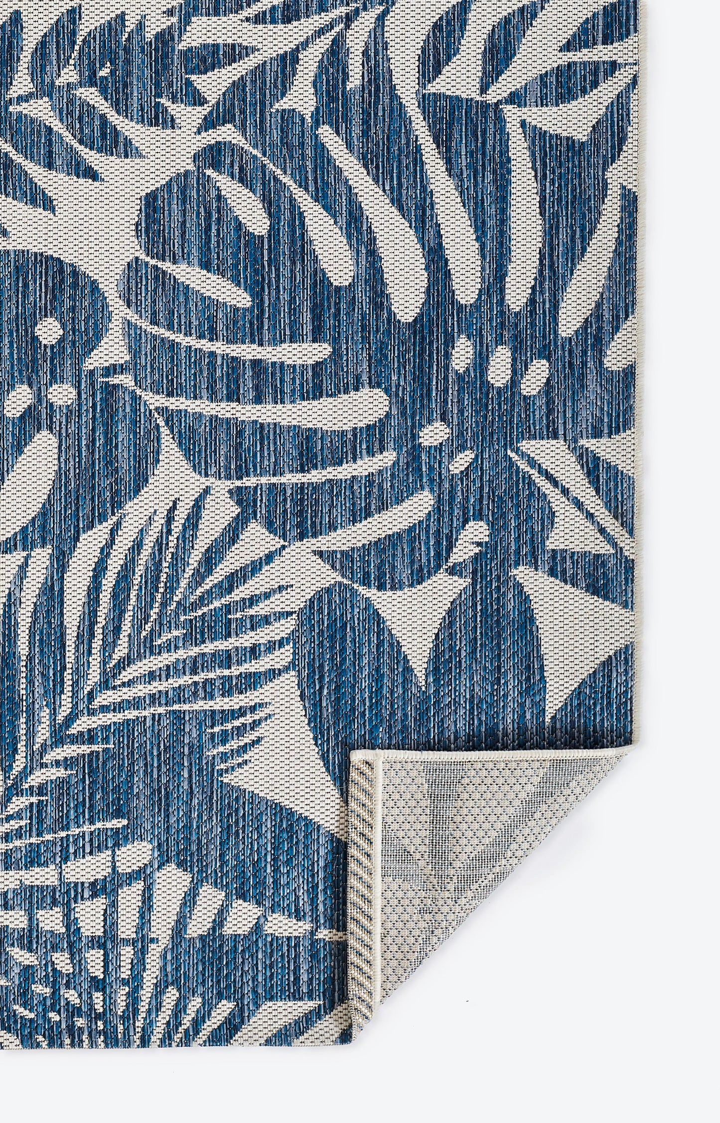 Blue tropical leaf pattern rug runner with white leaves, denim-like weave, folded at the corner.