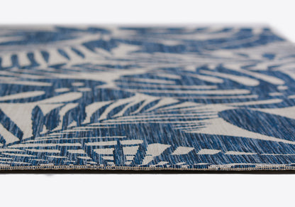 Blue and white woven runner rug with tropical leaf pattern, close-up edge detail.