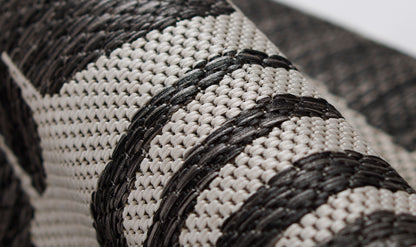 Macro close-up of beige natural straw weave with bold black braided stripes on a boho chic rug.
