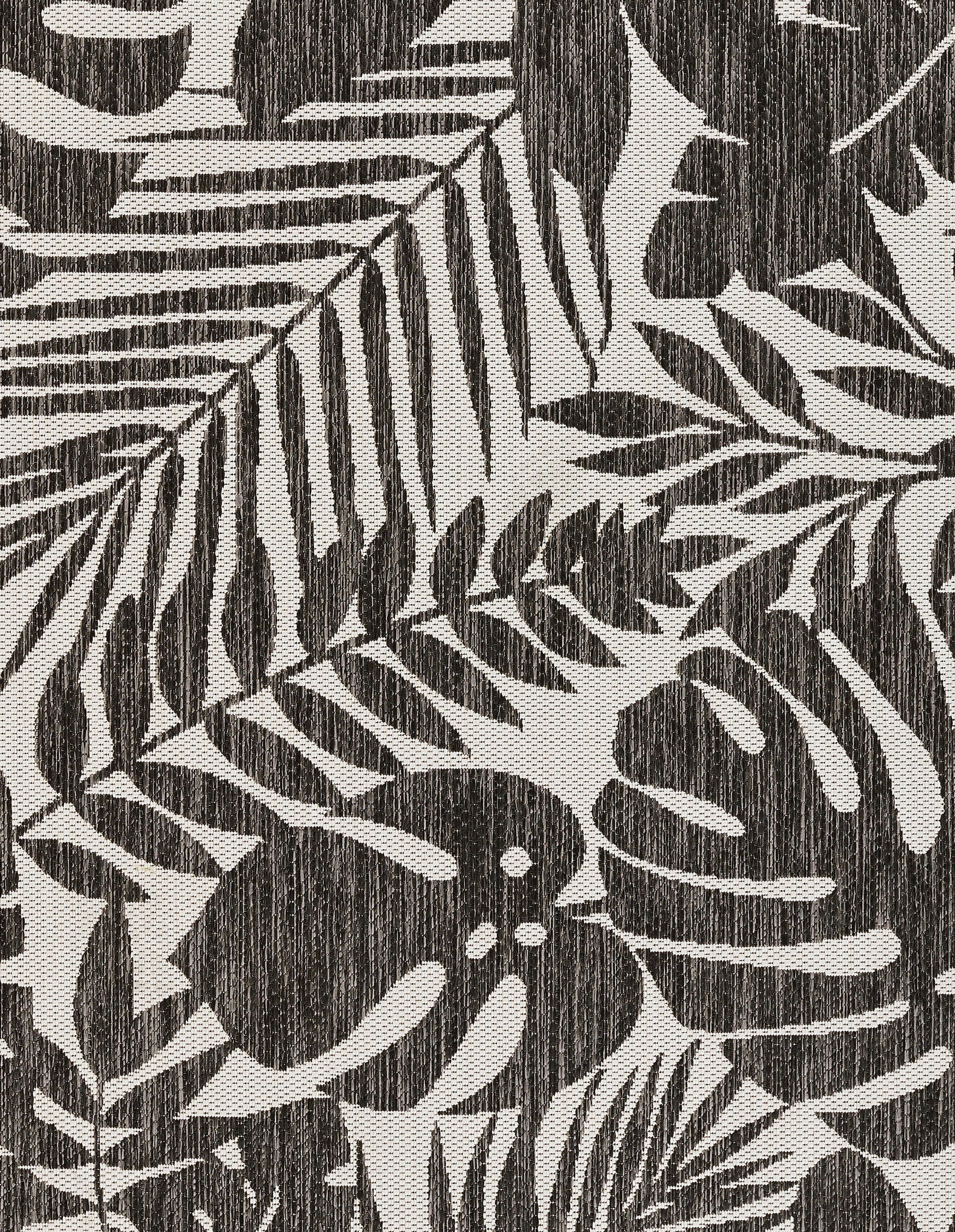 Charcoal rug with cream botanical leaf pattern of palm and fern fronds; textured woven look.
