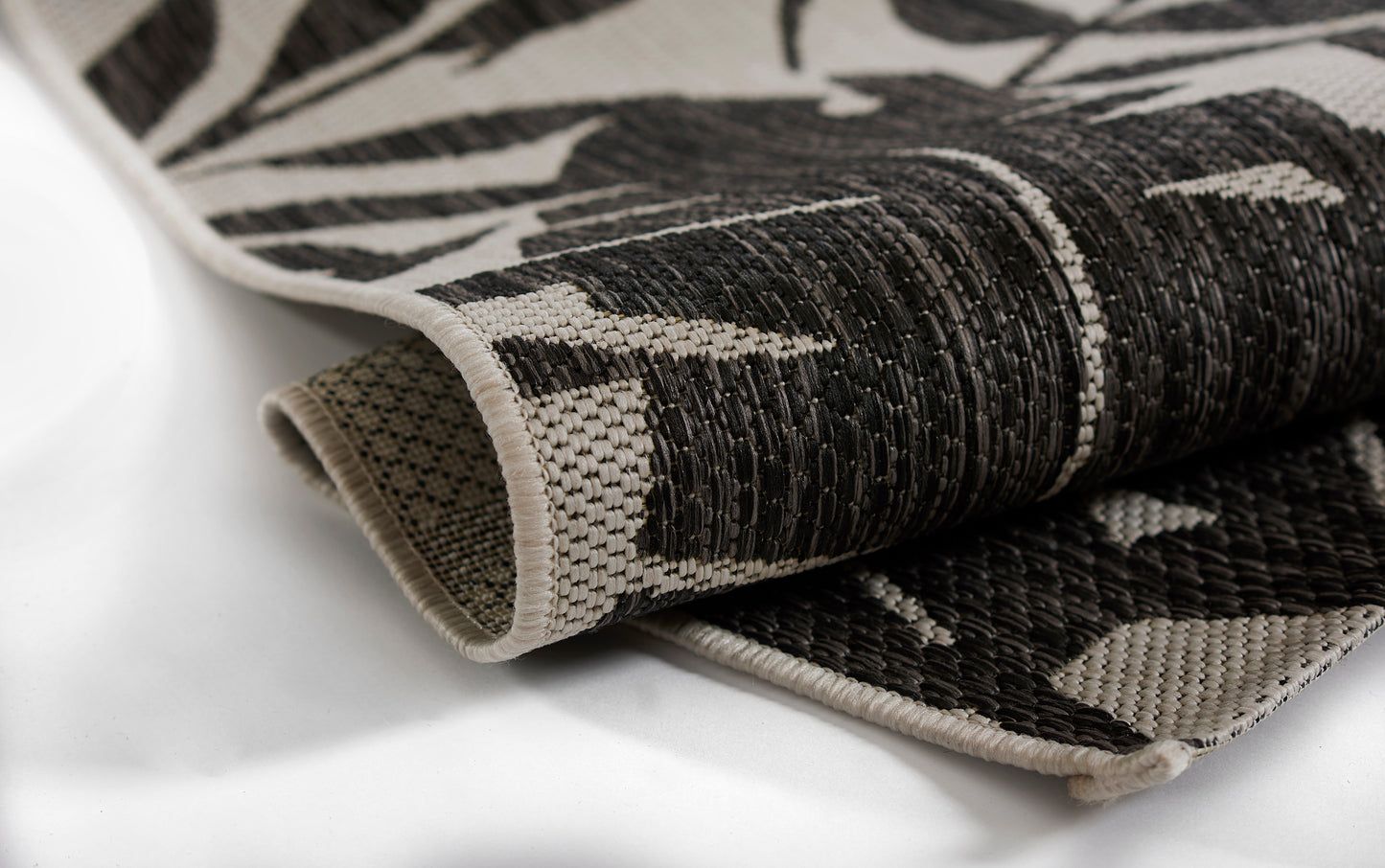 Rolled black-and-ivory woven rug with abstract botanical pattern, thick textured weave and beige edging.