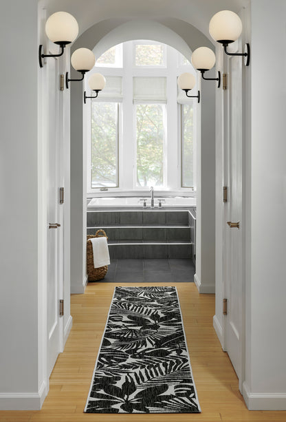 Hallway with black metal globe wall sconces and frosted globes, light wood floors, leaf-pattern runner rug, leading to a bright bath.