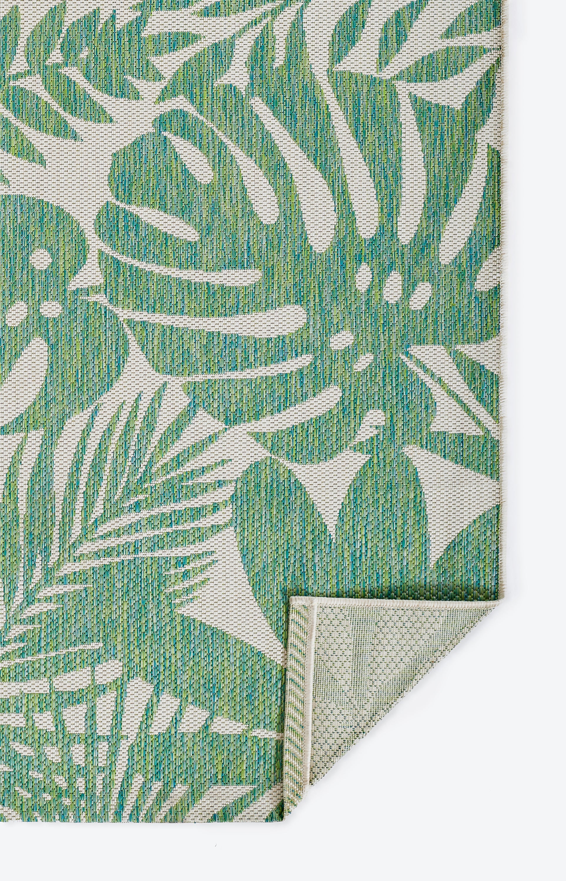 Green tropical leaf print on beige woven fabric; textured rug or mat with folded corner showing light underside.