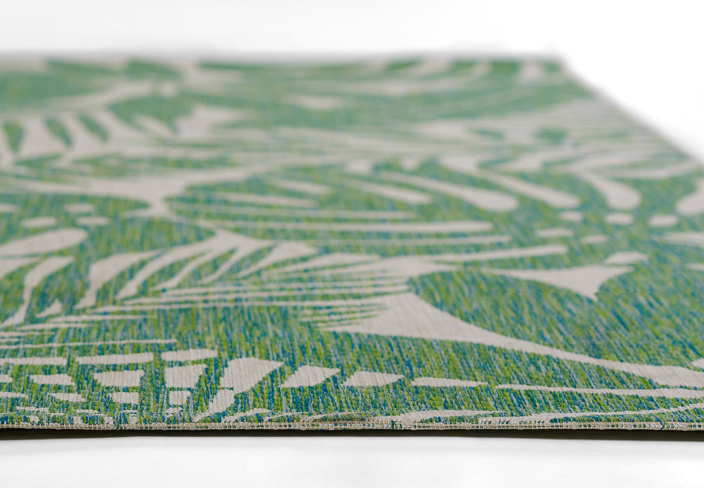 Green palm-leaf patterned woven rug, close-up edge view.