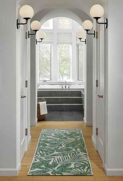 Green botanical leaf rug on warm wood floor in a white hallway with an arched doorway and globe wall sconces.
