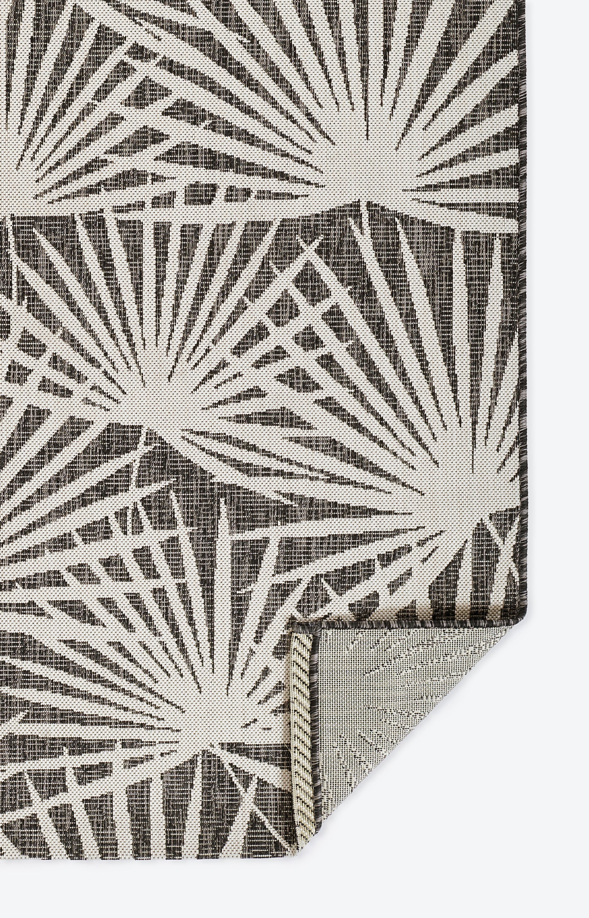 Charcoal gray rug with white sunburst print; woven texture with folded corner showing lighter reverse; size 2' x 3'.