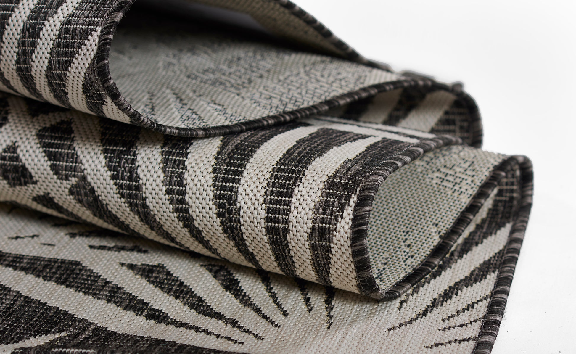 Rolled zebra-pattern rug in black and beige woven fabric, bold striped decor textile.