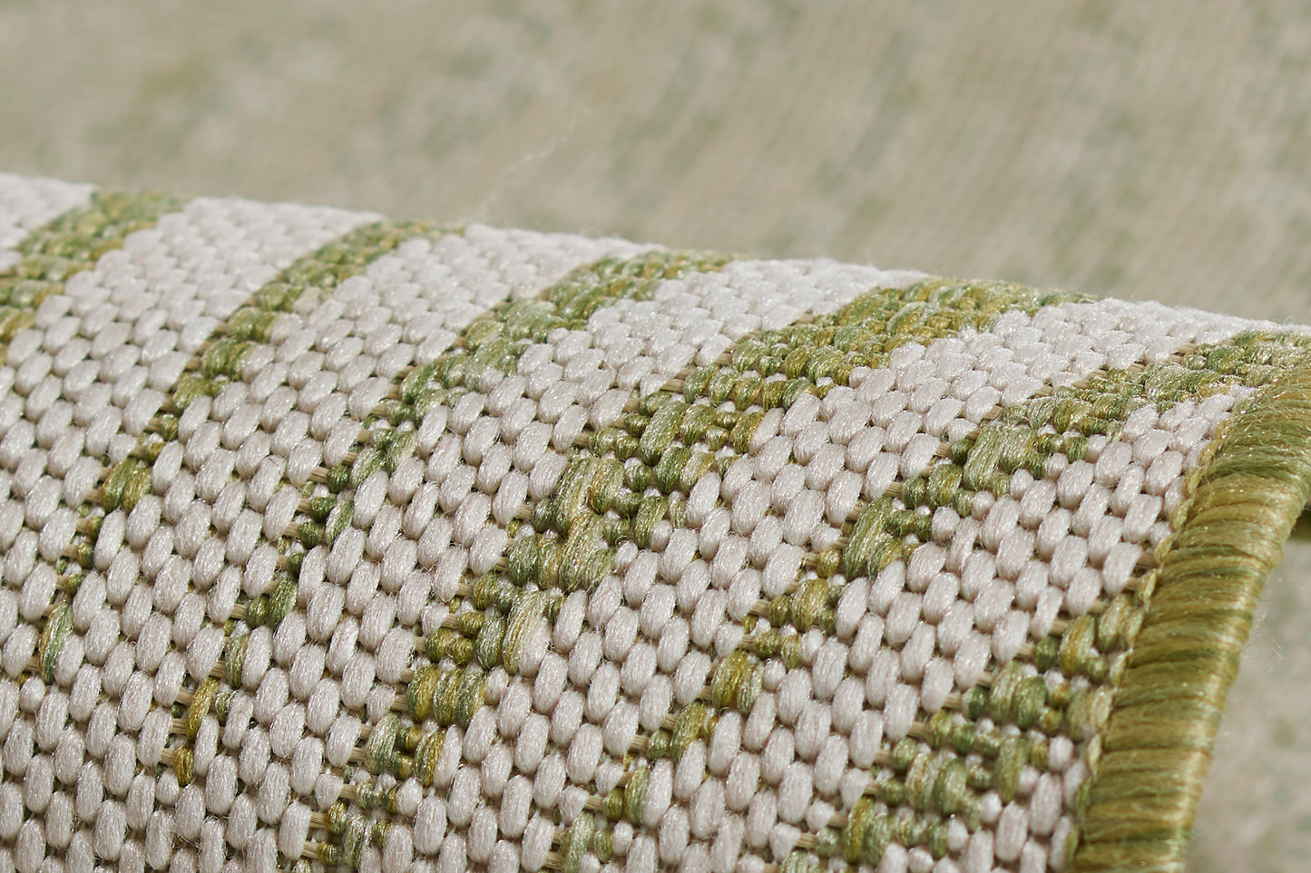 Close-up of a woven beige & green striped rug with textured weave & green fringe.