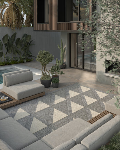 Modern outdoor patio with gray sectional seating, geometric gray-and-white triangle rug, potted plants, and wood accents.