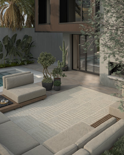 Modern outdoor lounge with beige modular sofas, grey rug, wooden base, concrete wall, glass doors, pool & potted plants.