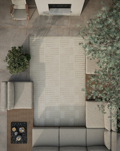 Outdoor beige sectional sofa with cushions around a geometric light rug; wood slat coffee table with a fire pit and greenery.
