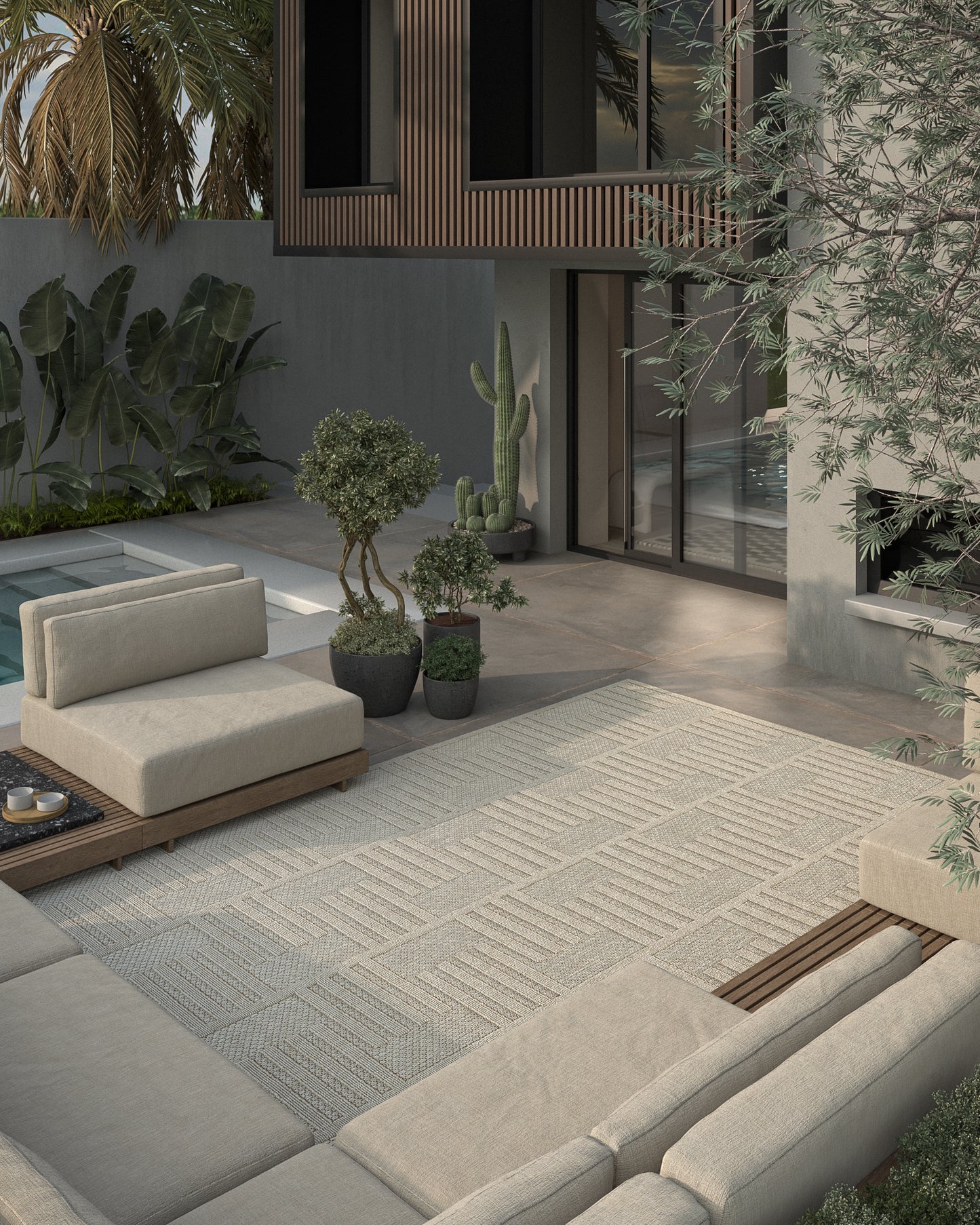 Contemporary outdoor lounge with beige sectional on a woven gray rug, wooden deck, potted cacti, and modern villa facade.
