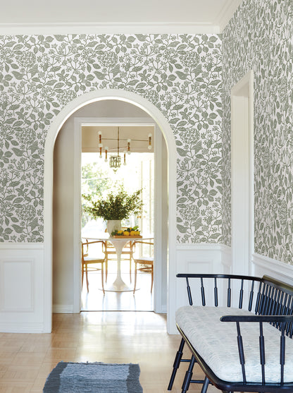 Arched doorway to bright dining area; green botanical wallpaper, white paneling, light wood floor, black spindle bench with pale cushion.