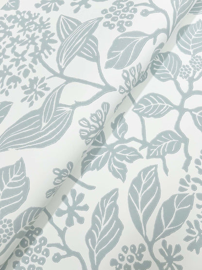Close-up of pale blue-gray botanical print on ivory fabric; leaves and clusters of small flowers.