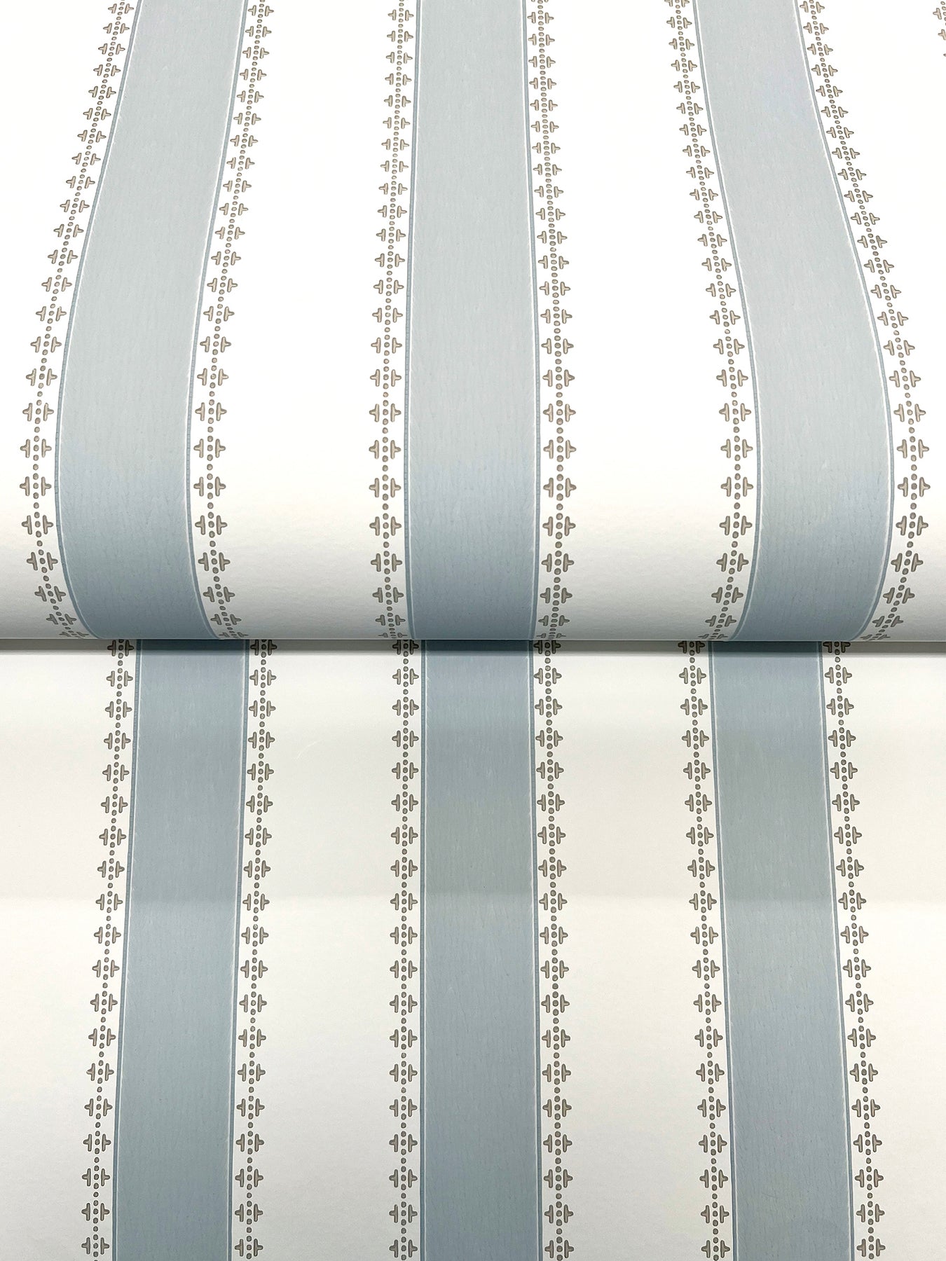 Wallpaper roll with pale blue-gray vertical stripes and delicate dotted borders on white background.