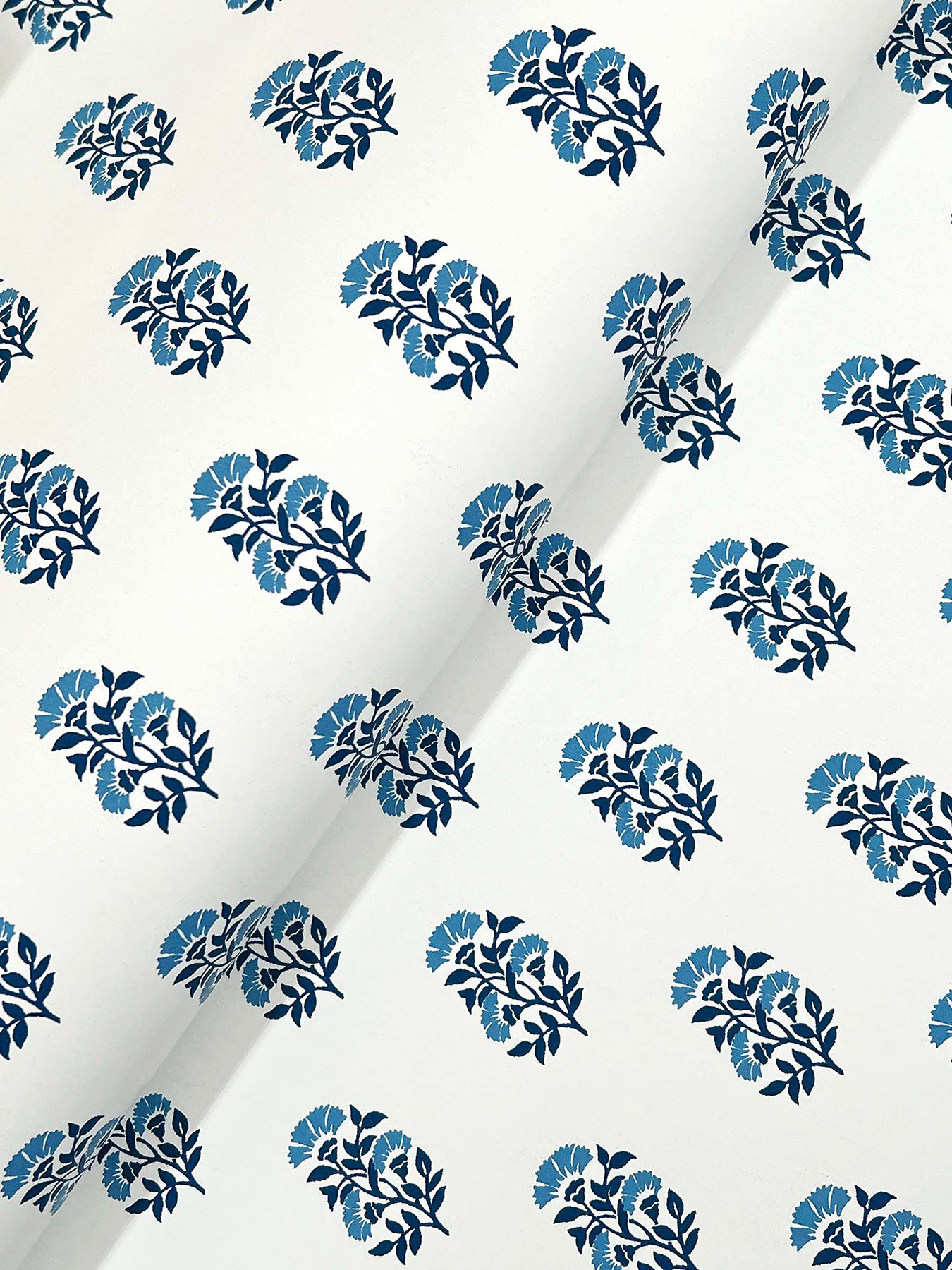 White fabric with repeating circular clusters of blue leaves in navy and light blue; diagonal crease across the print.