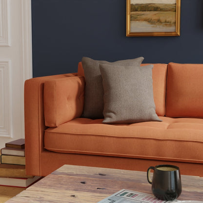 Orange fabric sofa with gray cushions on a dark navy wall; wooden coffee table with a mug and a newspaper.