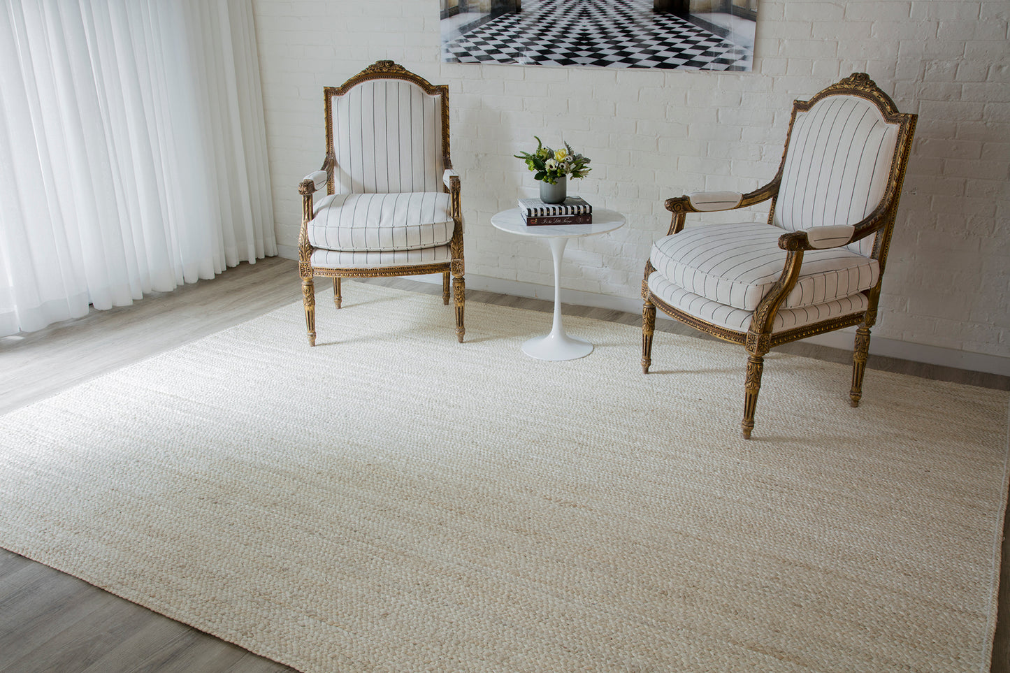 Two ornate carved-wood armchairs with striped beige upholstery beside a white round side table and a plant on a beige runner rug.