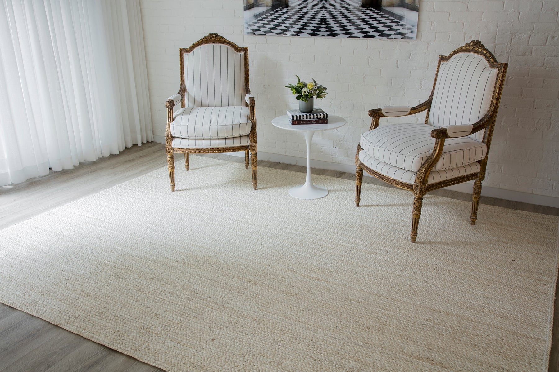 Two ornate carved-wood armchairs with striped beige upholstery beside a white round side table and a plant on a beige runner rug.