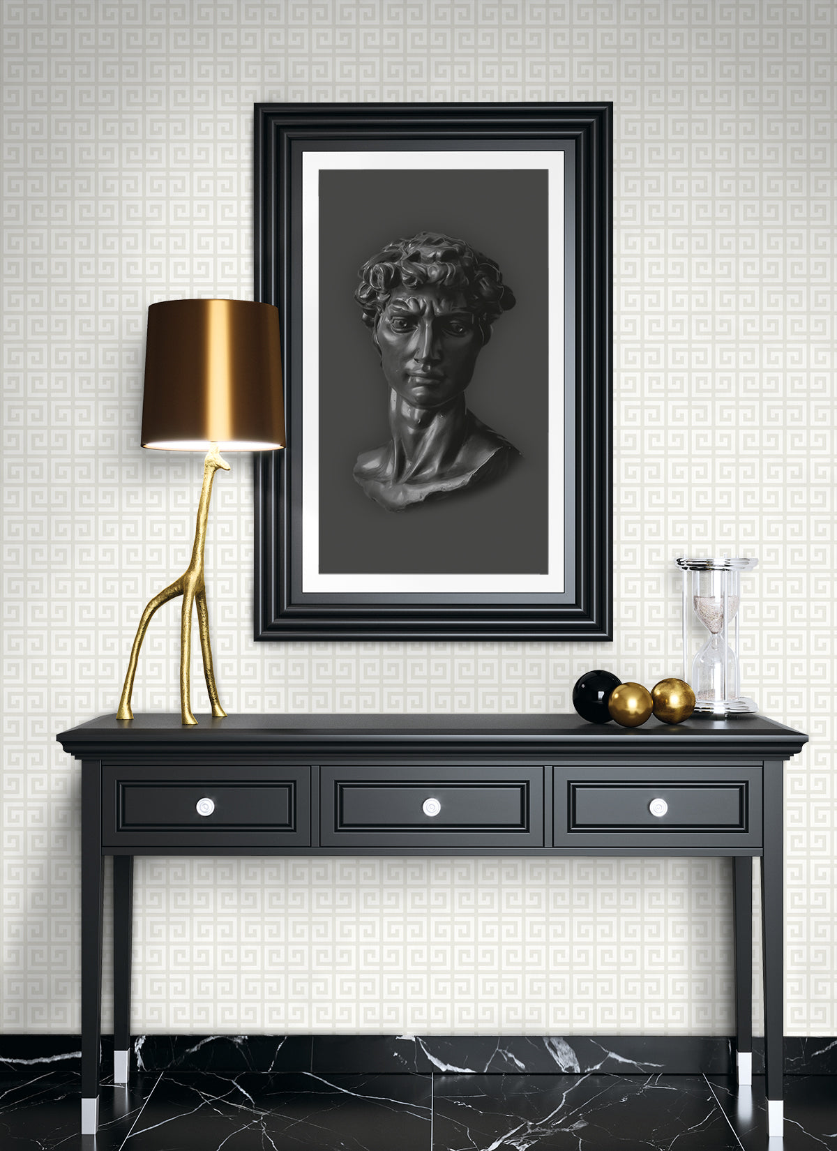 Dark console table with three drawers and silver knobs, brass branch lamp, framed grayscale bust art, and decorative spheres.