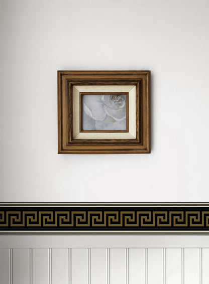 Square brown wood frame with cream mat and grayscale rose print, mounted above a Greek key border on a white wall.