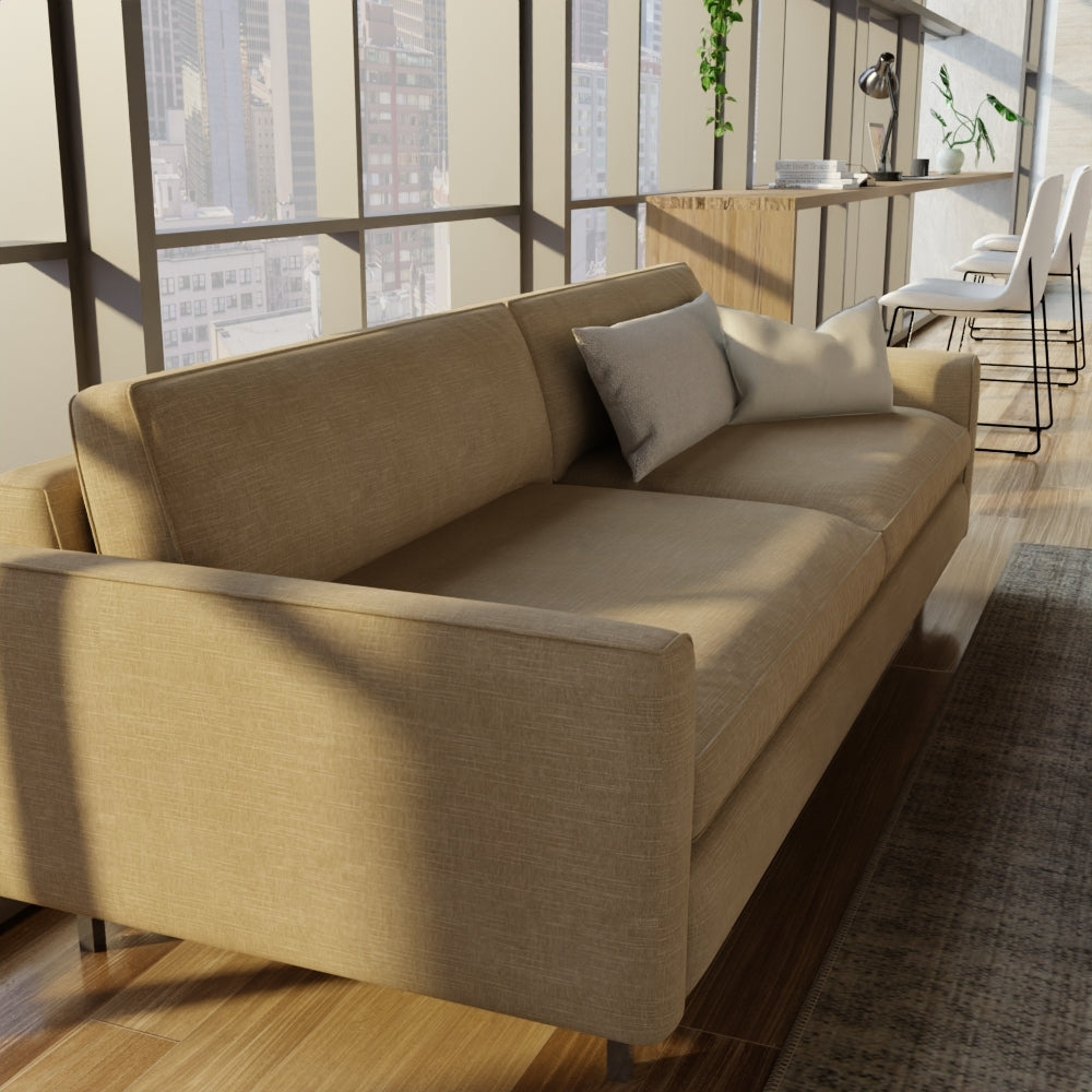 Beige limestone solid fabric upholstery on a sofa with square arms and two gray cushions in a sunlit loft with wooden floors and city-view windows.