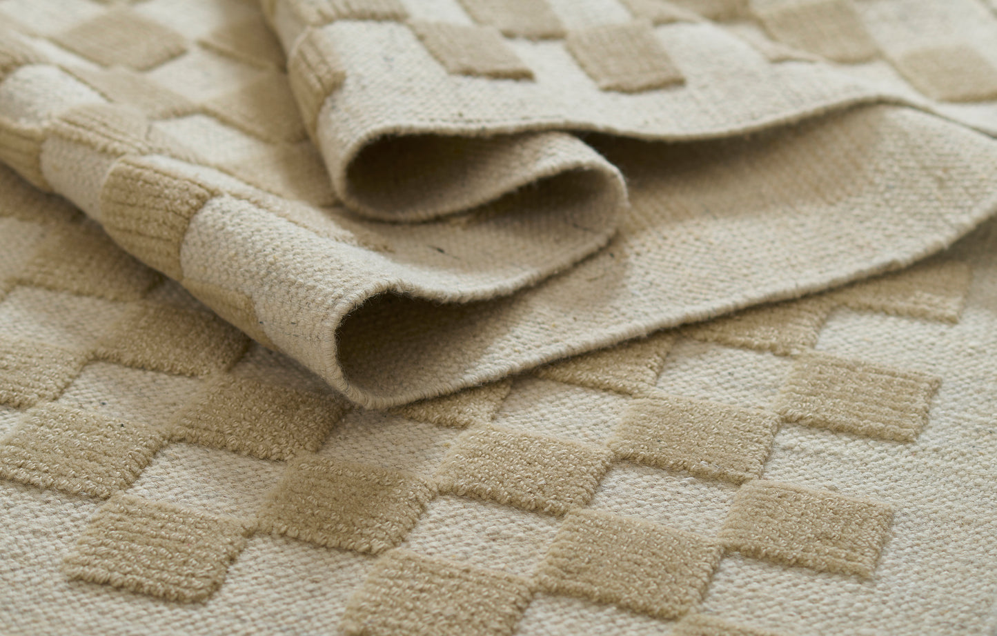 Beige rug with raised square pattern and soft terry texture, folded edge.