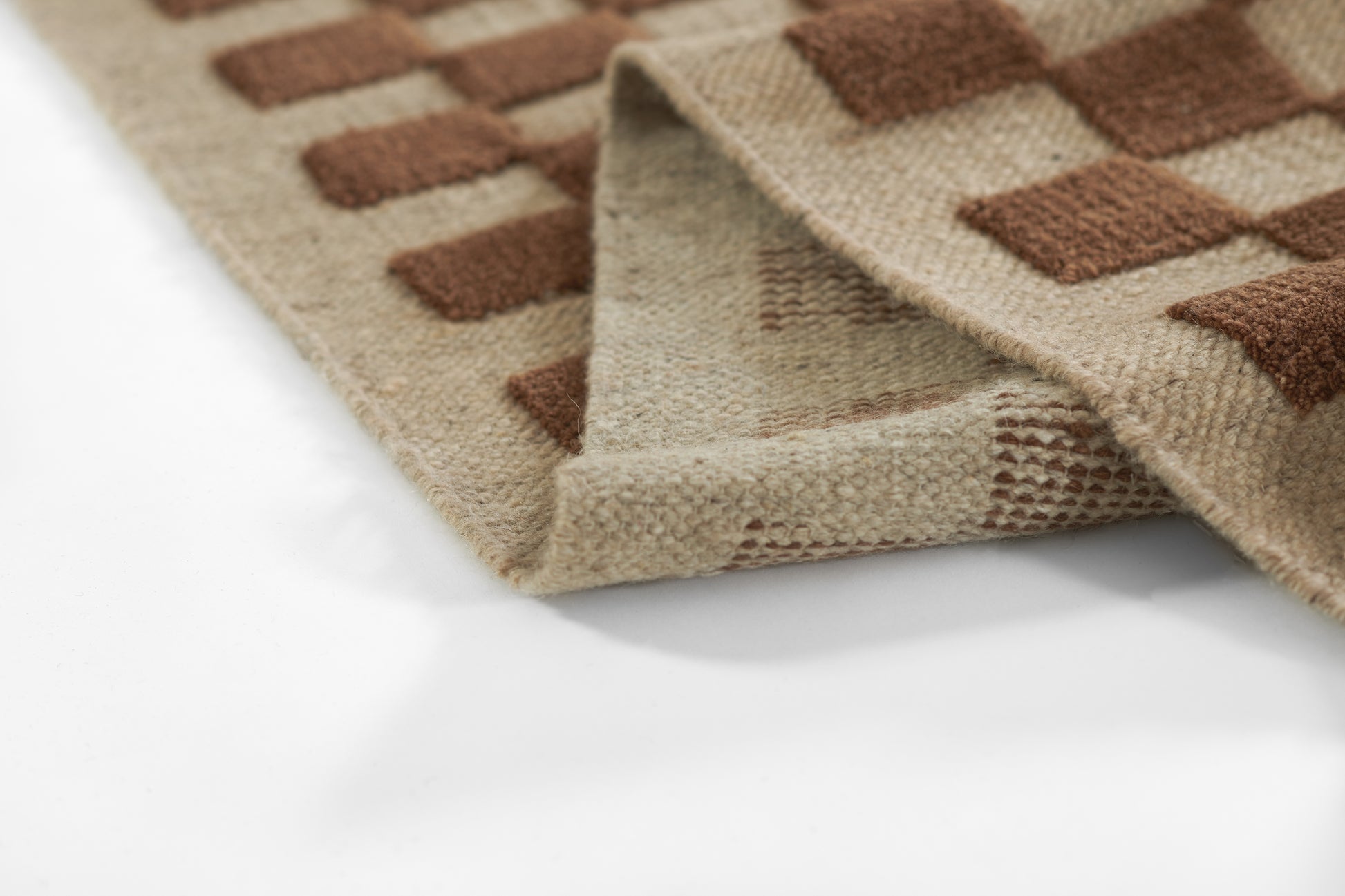 Beige and brown checkered woven rug with a folded corner, showing textured pile and soft weave. Size 10' x 14'.