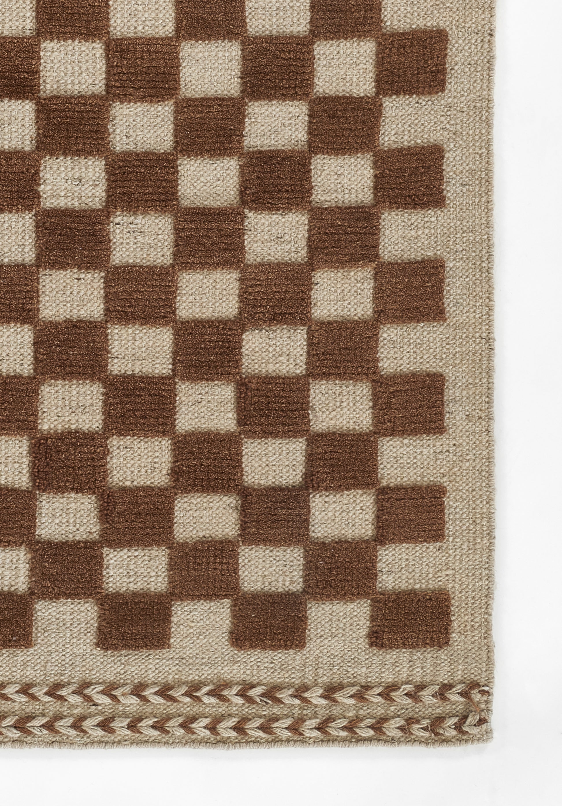 Beige woven rug with a brown checkerboard pattern and a decorative braided edge along the bottom.