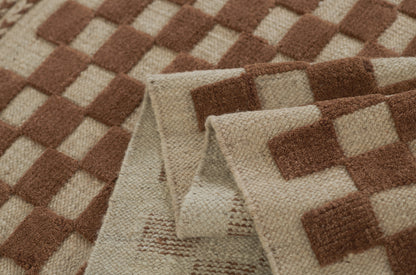 Brown and beige checkered woven rug with chunky texture and folded edges.