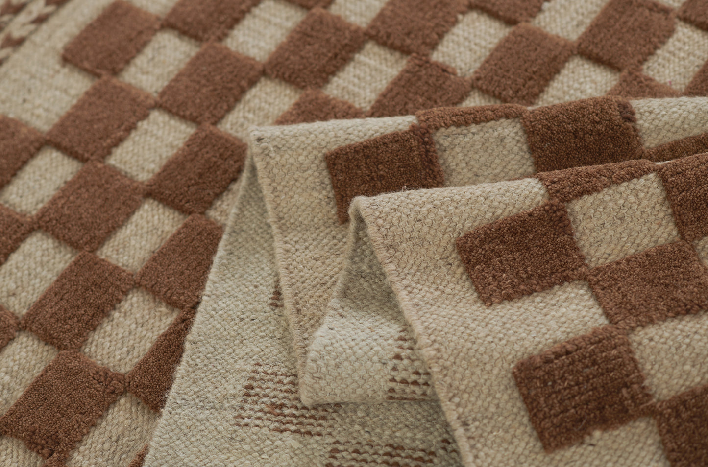 Brown and beige checkered woven rug with textured fibers and folded edge.