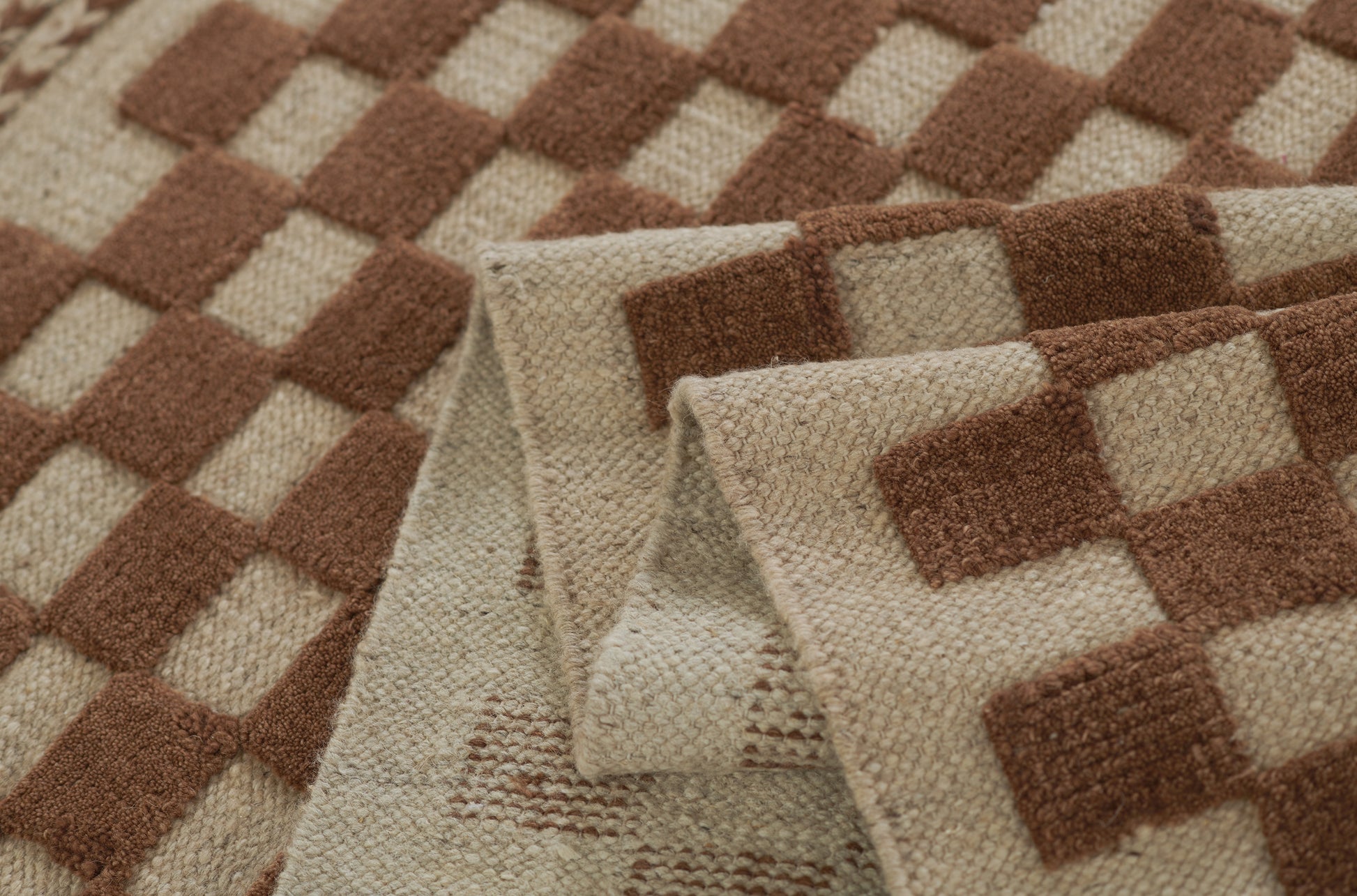 Brown and beige checkered woven rug with textured fibers and folded edge.