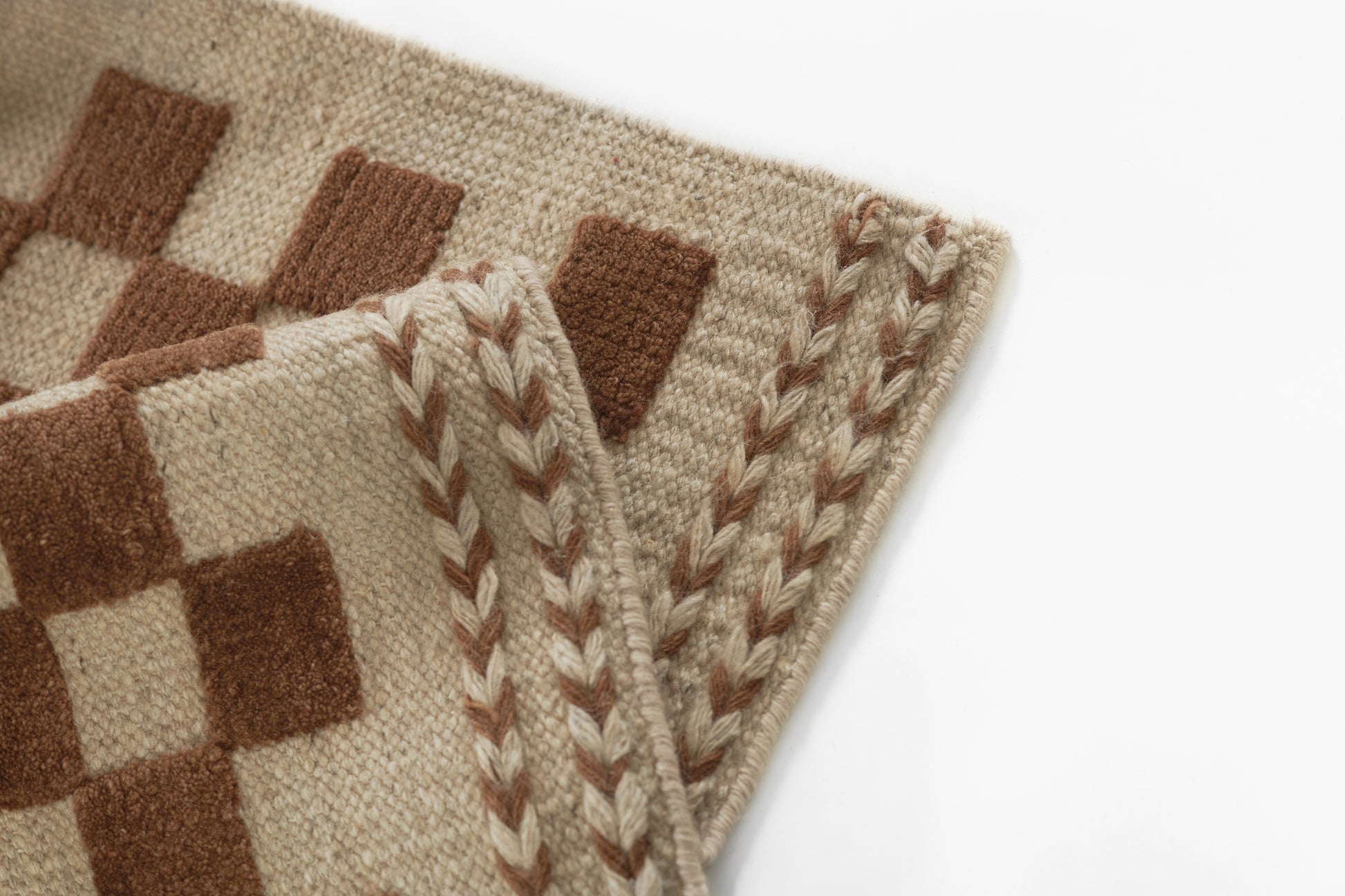 Beige woven rug featuring brown checkerboard squares and braided edge trim.