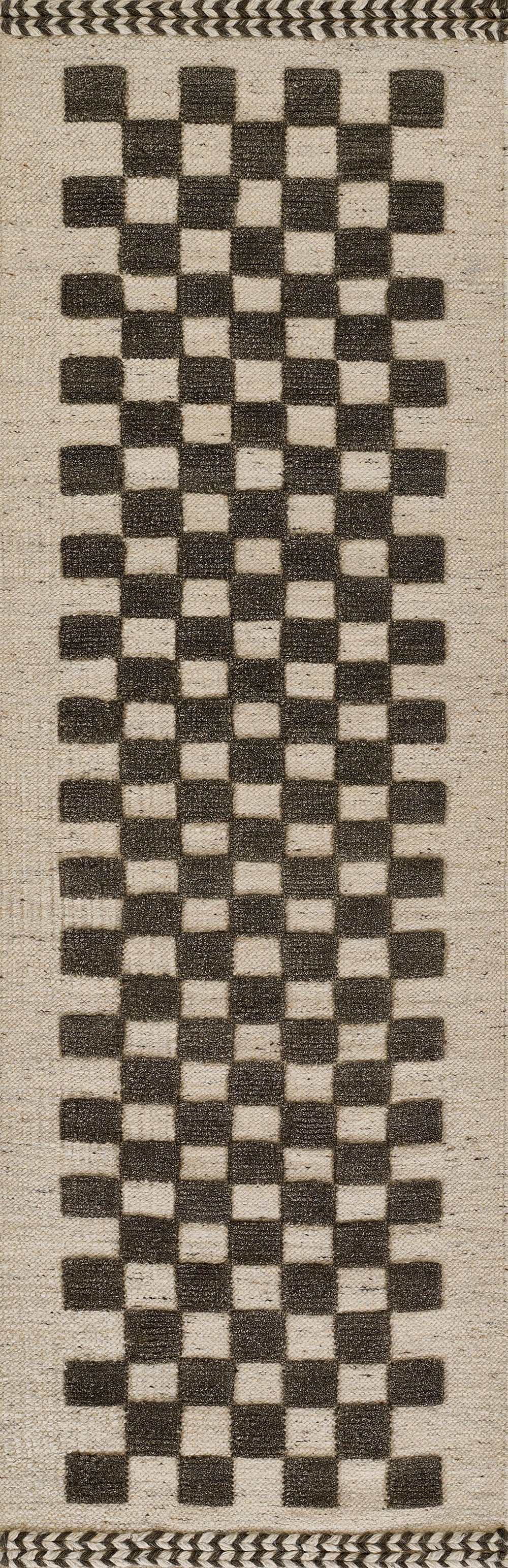 Natural beige woven rug with a tall vertical stripe of black checkerboard squares; rustic boho rug trim.