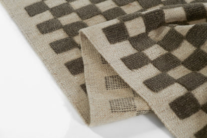 Beige woven rectangular throw rug with dark brown checkerboard pattern; natural fiber look, cozy home decor.