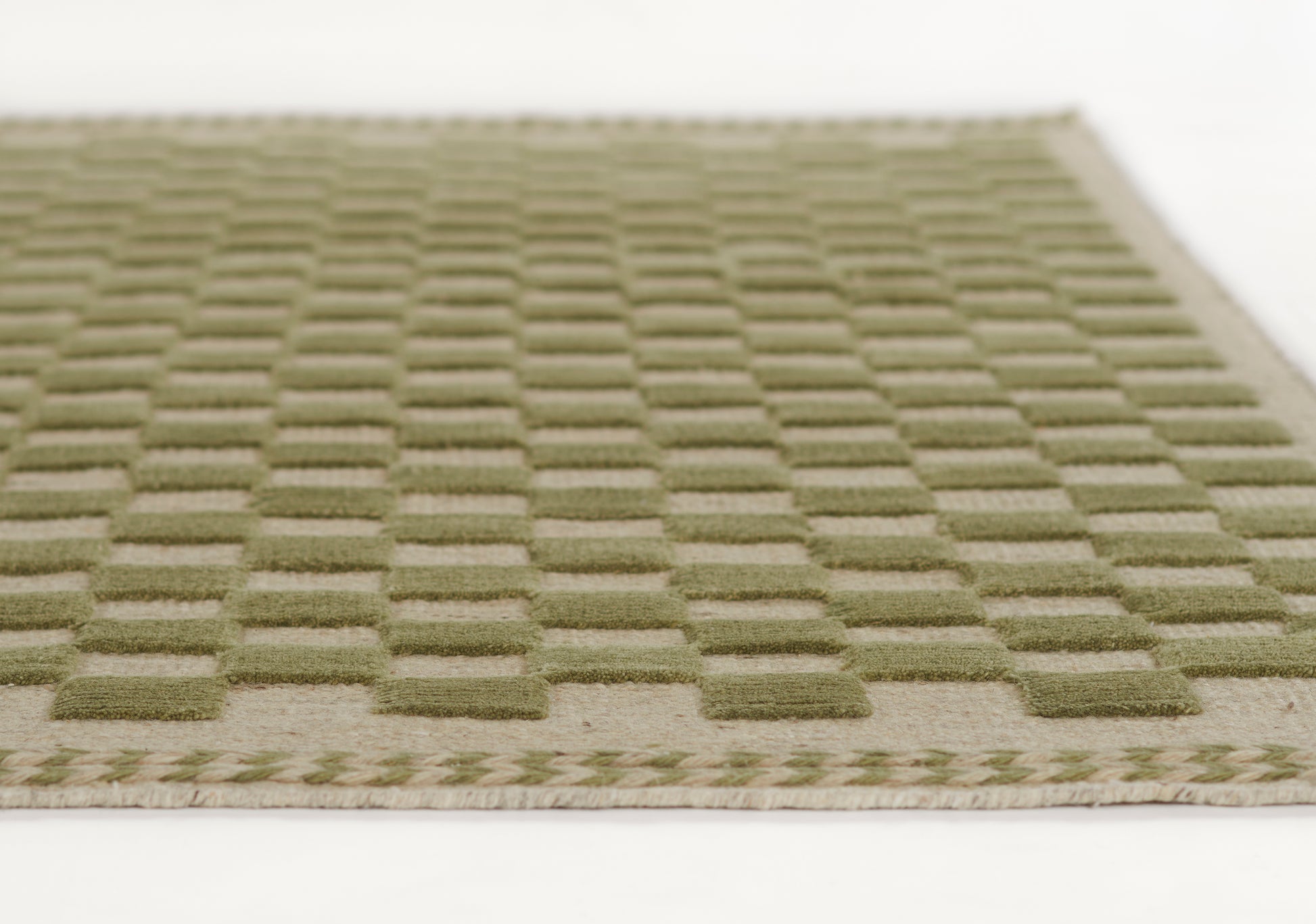Olive green flat-weave rug with a raised grid-square pattern and beige border.