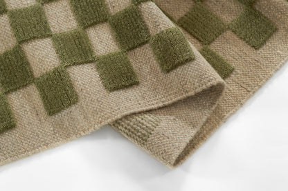 Close-up of a beige woven runner rug with an olive green square grid pattern; folded edge.