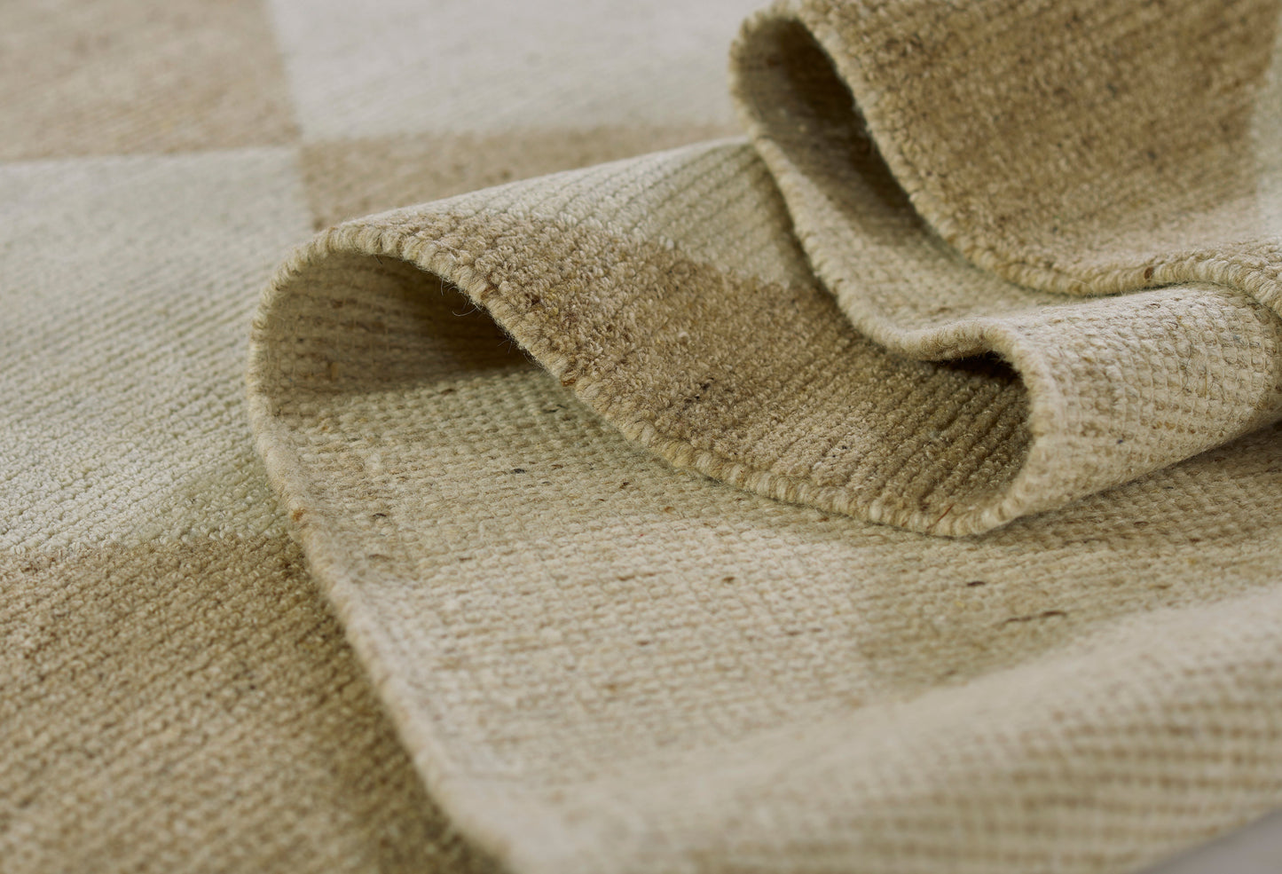 Beige woven jute rug close-up; natural fibers, checkered pattern, folded edge and coarse textured weave.