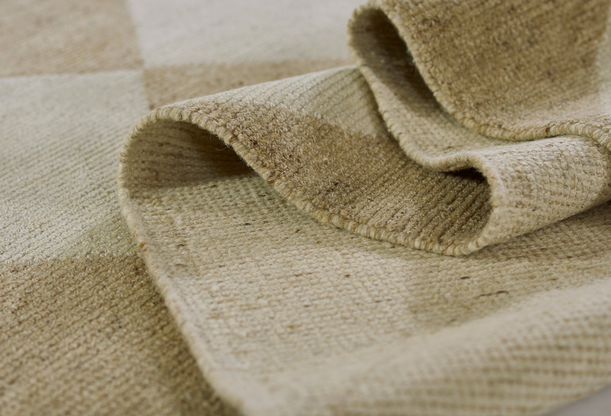 Beige woven jute rug close-up; natural fibers, checkered pattern, folded edge and coarse textured weave.