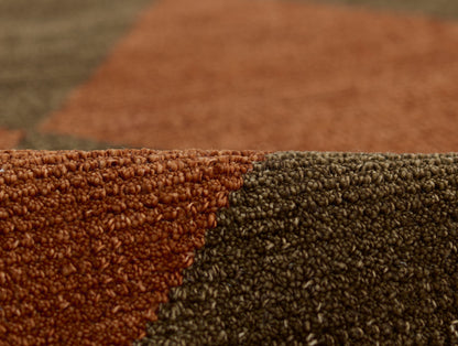Close-up of a color-block rug with rust orange and dark brown loop-pile texture.