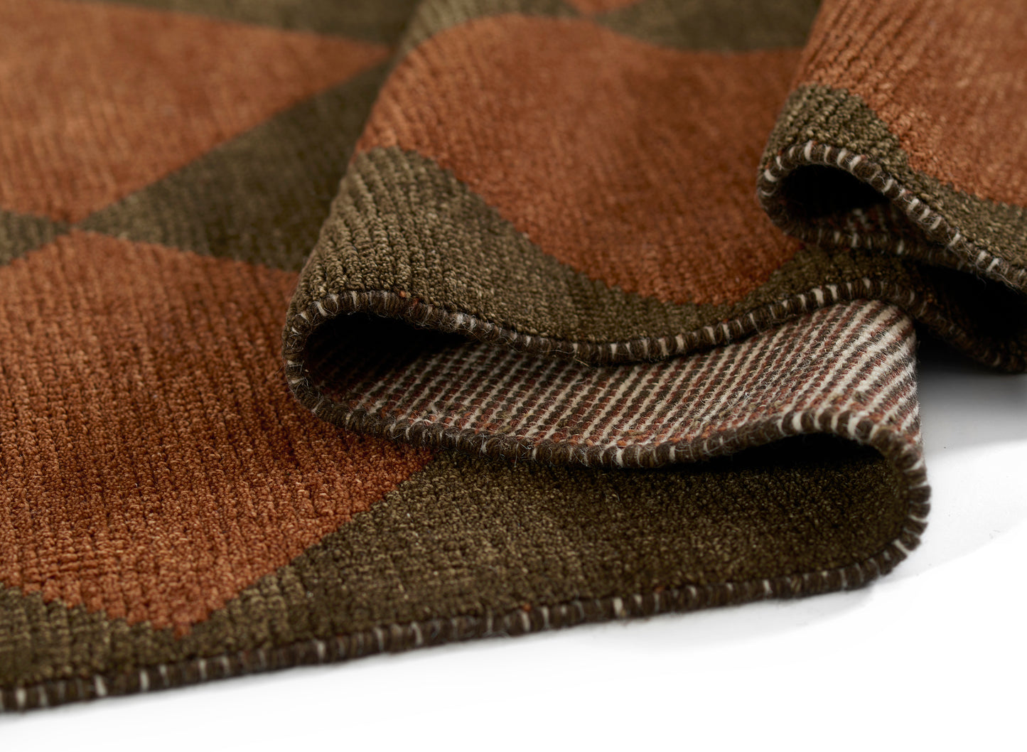 Orange-brown and olive plaid wool rug with a chunky woven texture, softly folded to reveal a striped underside edge.