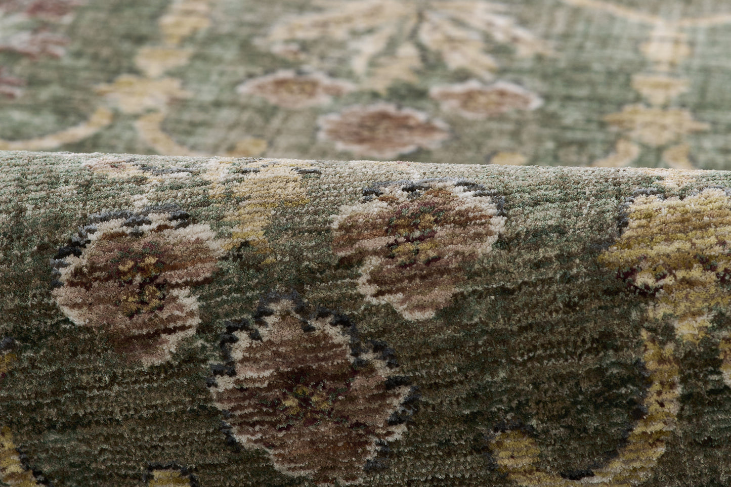Close-up of green floral area rug with brown-beige medallions and textured pile.