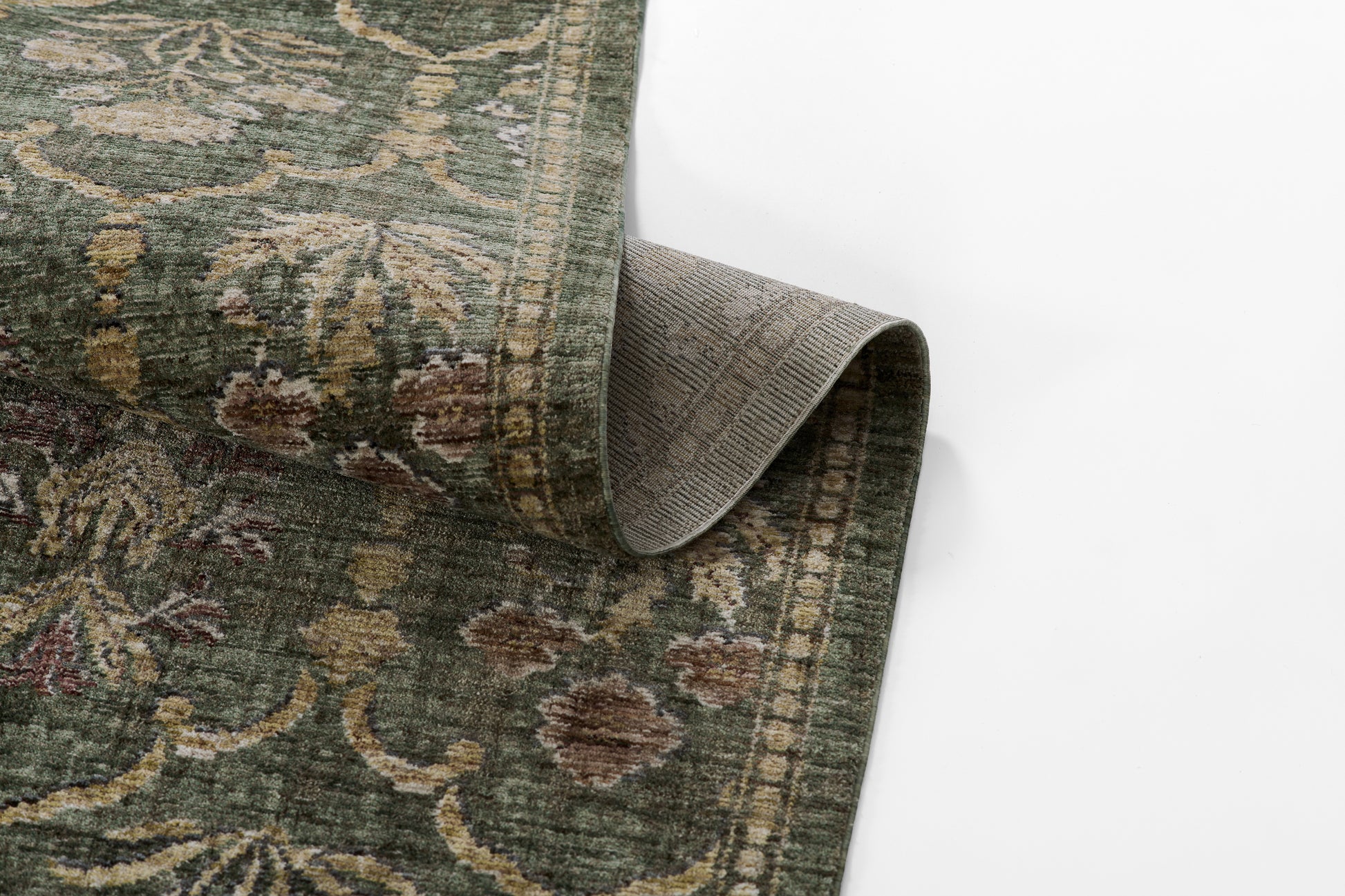 Green traditional floral area rug with beige and brown motifs, rolled corner revealing gray backing.