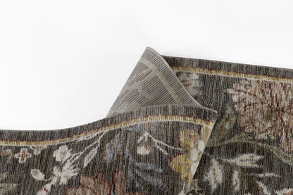 Dark floral woven rug with muted browns, beiges, maroons & greens; thick wool pile & folded corner.