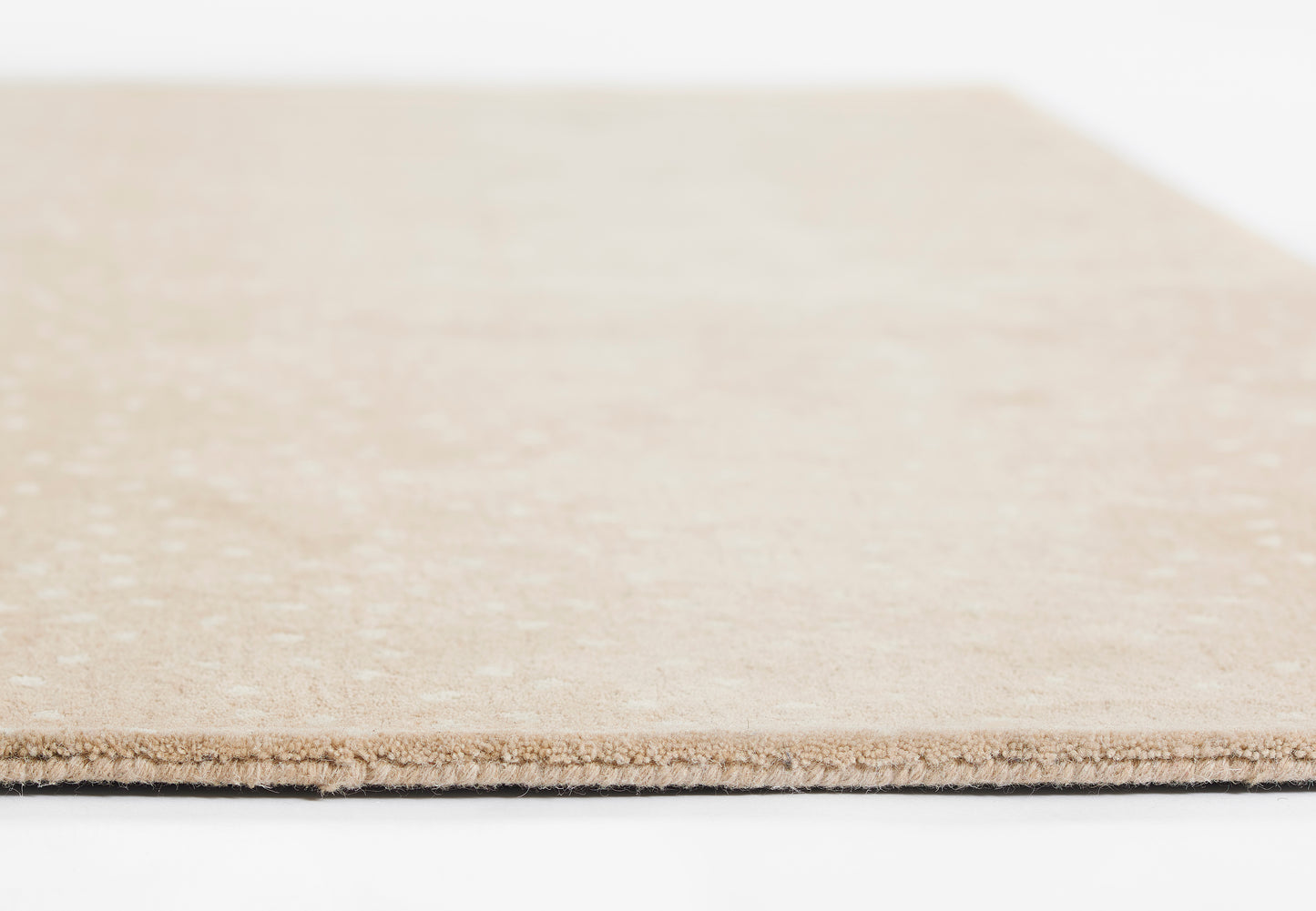 Close-up of a light beige rug edge with visible fibers.