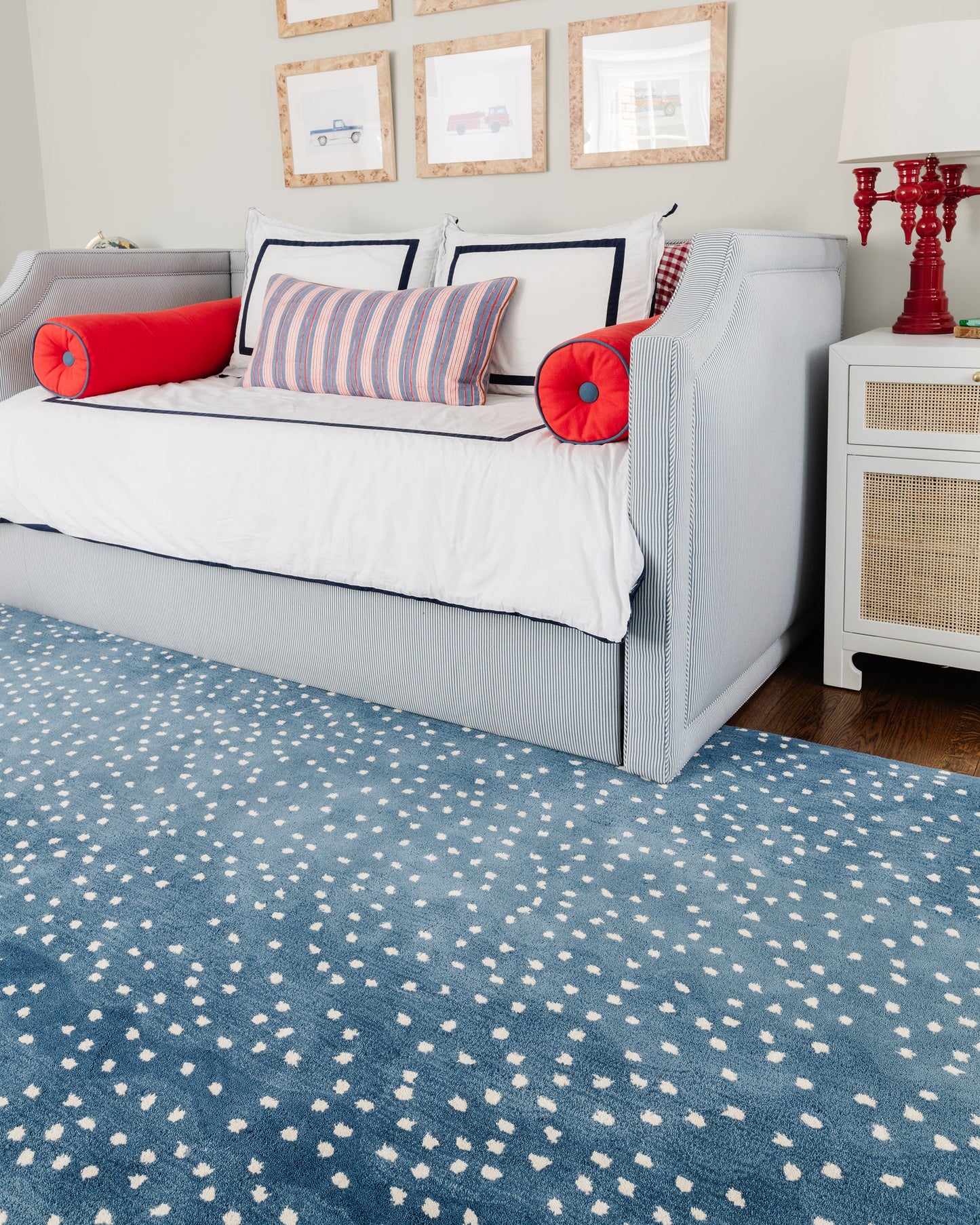 Blue rug on the floor in a coastal living room; a light gray-blue sofa with white cushions, red bolster pillows, and navy striped cushions nearby.