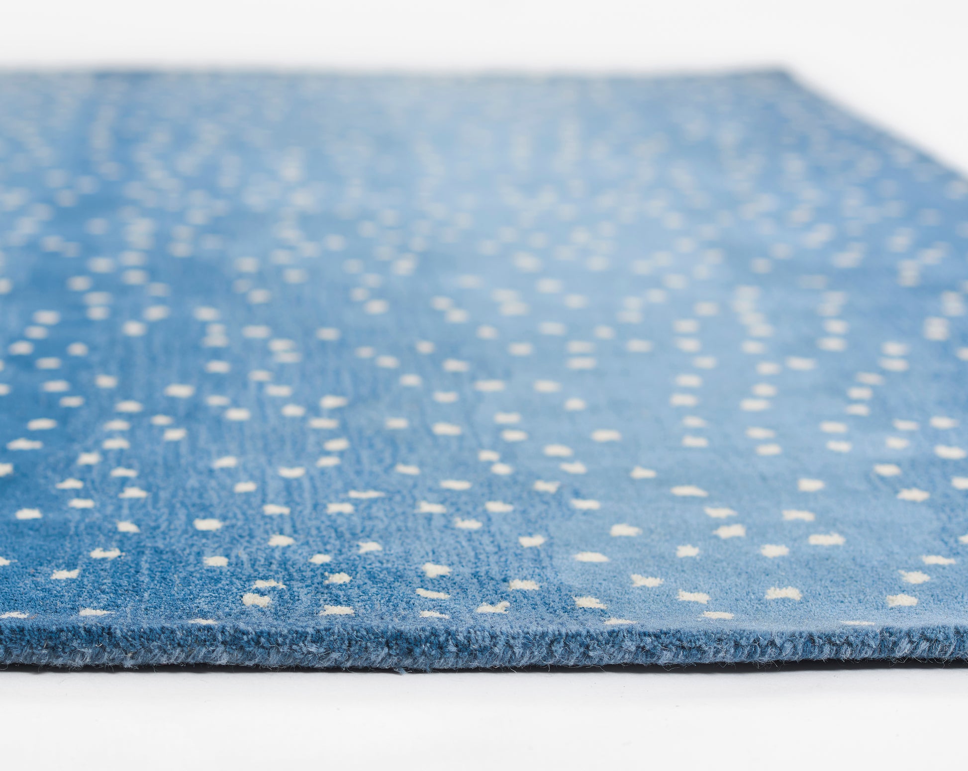 Blue area rug with white dotted specks, low-pile weave, rectangular modern-style rug.